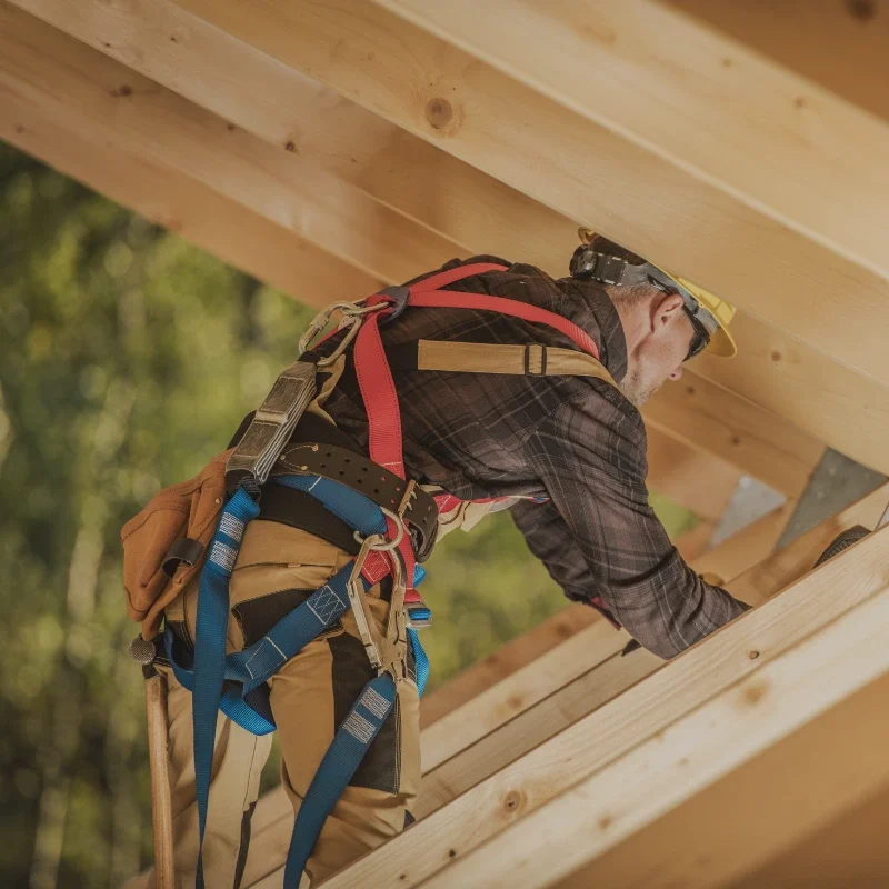 Doświadczony cieśla w uprzęży bezpieczeństwa podczas montażu więźby dachowej.