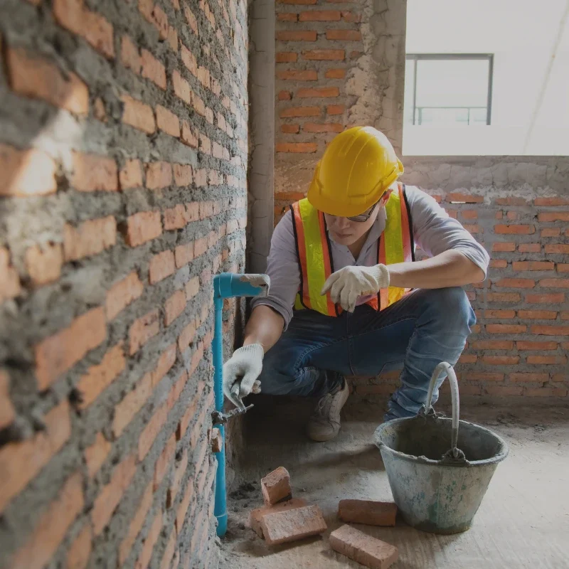 Murarz wykonujący prace przy ścianie z cegły wewnątrz budynku.